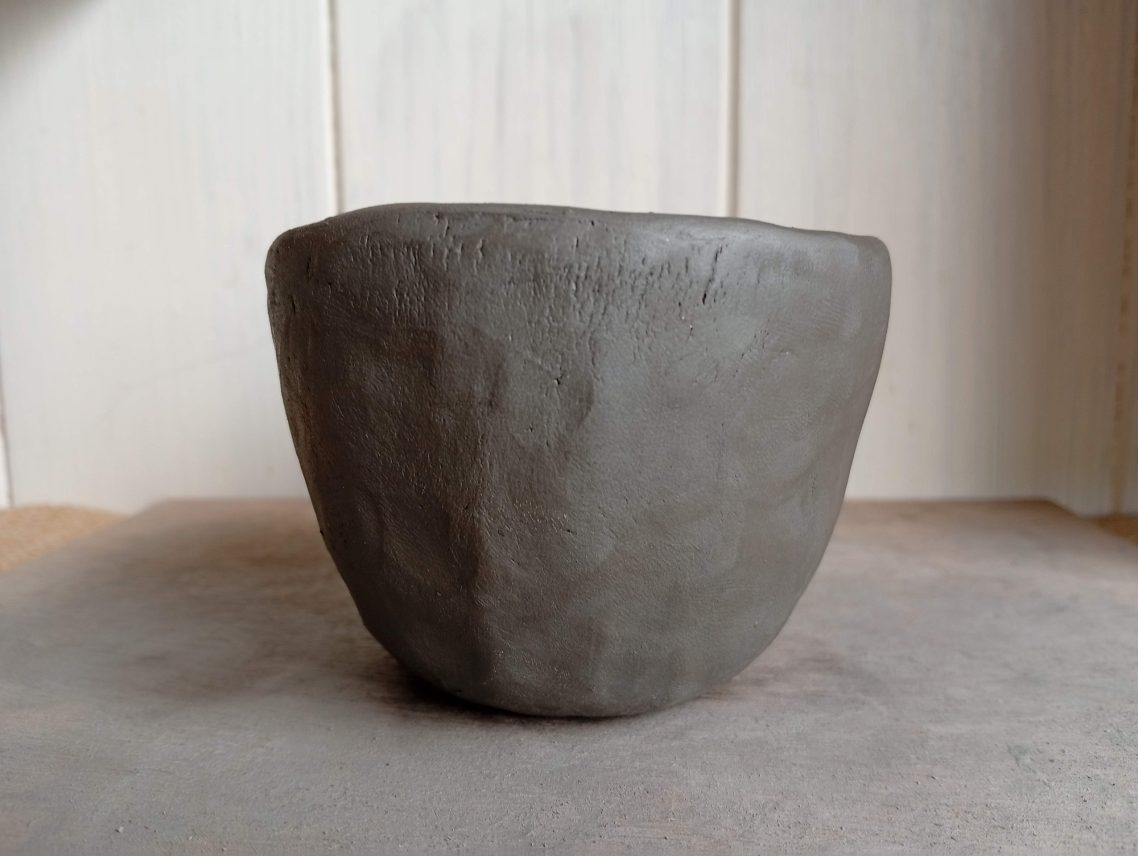 Tasse fraichement modelée Vase en argile de forme simple et grise, sur fond neutre.